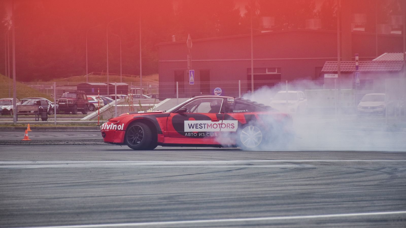 A red drift car sliding sideways and producing a thick cloud of tyre smoke on a motorsport track