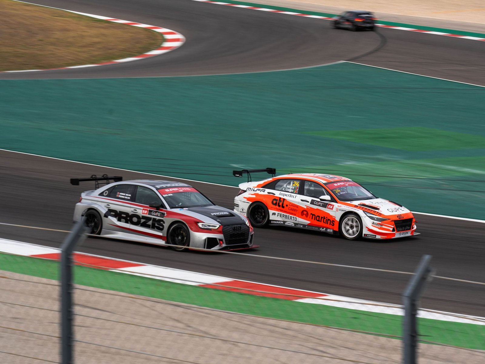 Two race cars battling at high speed on a coastal motorsport circuit