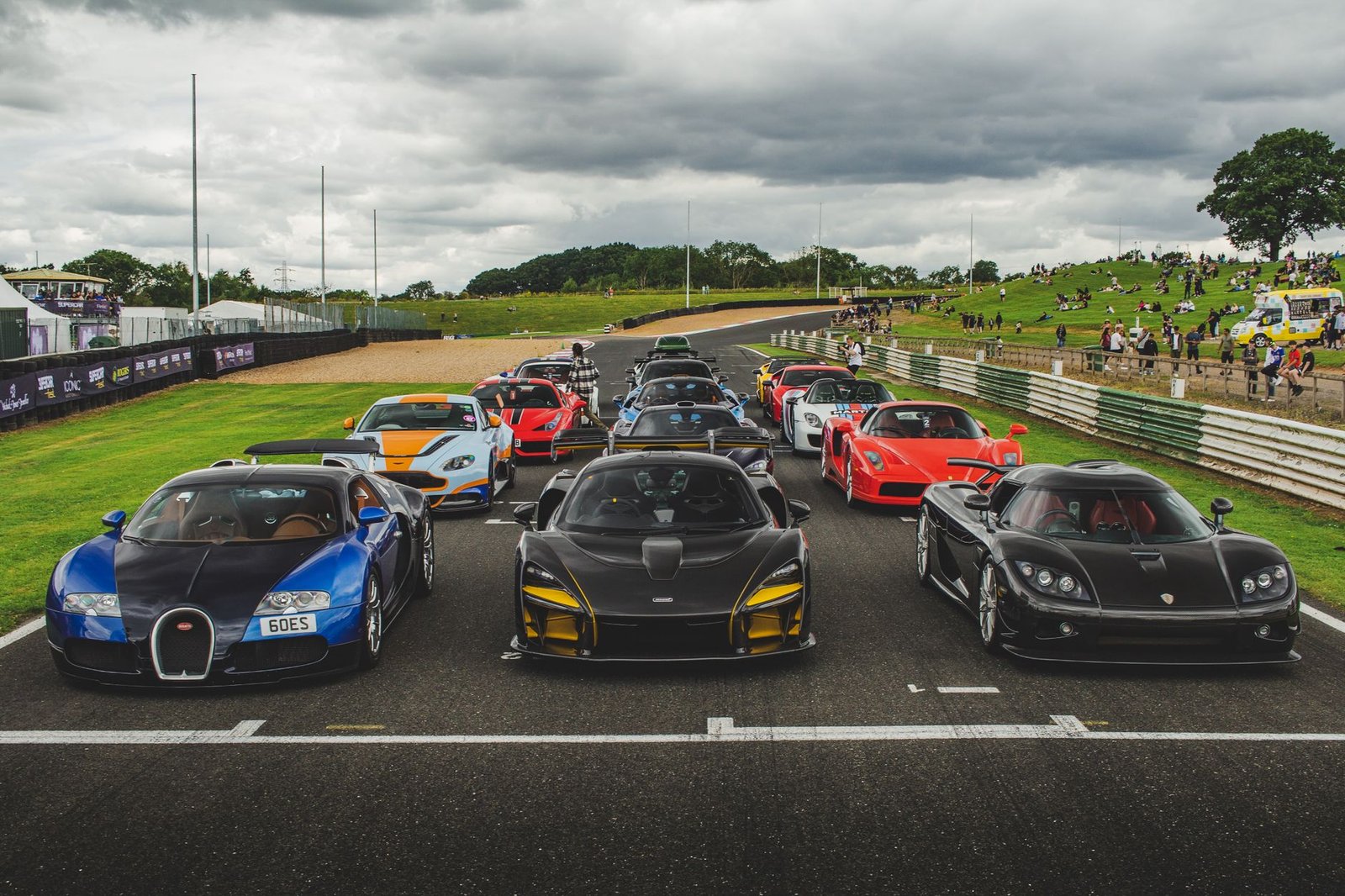 A lineup of luxury supercars ready for a track event at an outdoor racing circuit